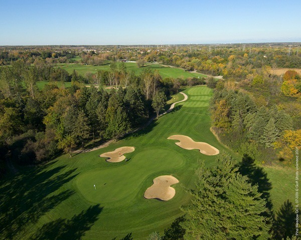 Aerial view of Hole 12 green and fairway lined by trees and 3 sand traps around the green