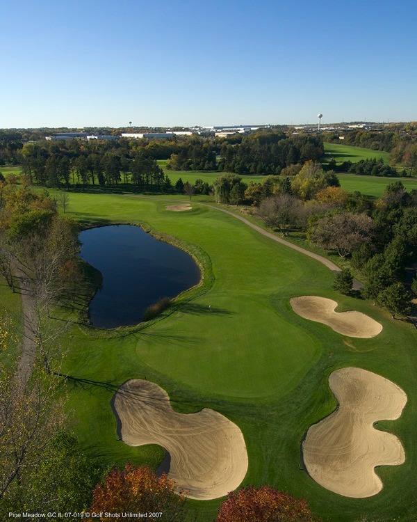 Aerial view of Hole 18, with a sand trap surrounded green leading out into the fairway with water hazard on the side
